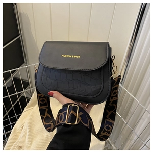 Detail of black saddle bag with crocodile texture, wide strap and gold lettering