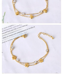 Detail view of double-layered gold chain bracelet with heart, flower, and zircon charms