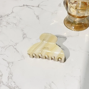 Creamy beige acetate hair claw clip with marble texture on white stone background