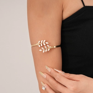 Detailed view of a gold leaf arm cuff featuring white enamel inlay on a female model