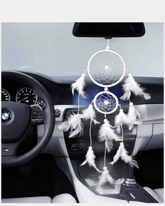 Detail view of a white dream catcher with soft feathers hanging from a car rearview mirror