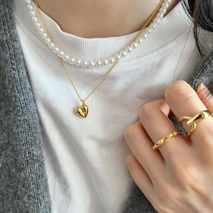 Golden 3D heart pendant necklace paired with minimalist pearl choker on a female model