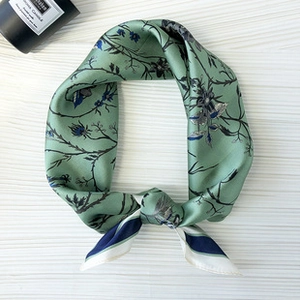 Close-up of knotted green silk scarf with dark floral patterns and blue striped edges