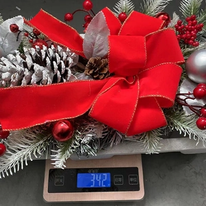 Detailed view of artificial Christmas wreath with red bow and pine cones on a digital scale