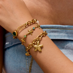 Close-up of golden layered starfish bracelet set with colorful zircon and green heart charm