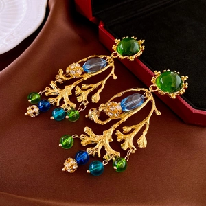 Gros plan sur boucles d'oreilles baroques dorées avec pierres vertes et cristaux bleus