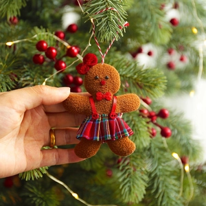 Gingerbread man ornament with red bow and plaid skirt on a lit Christmas tree