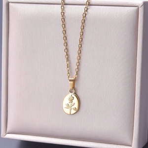 Macro detail of oval gold rose embossed pendant on a fine link chain necklace