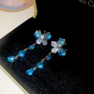 Macro shot of butterfly drop earrings with blue crystals on black velvet display
