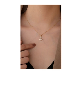 Close-up of golden anchor pendant necklace with sparkling stones on a model