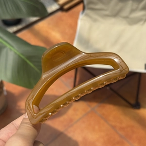 Detail of a 10cm amber perfume bottle hair claw clip held by hand in outdoor lighting