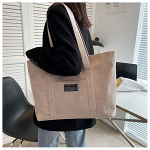 Side view of beige canvas tote bag with black fashion label on a female model
