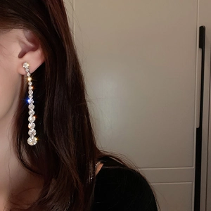 Close-up of long tassel earrings with sparkling crystals worn by a model in soft light