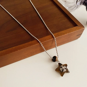Detail of star-shaped brown resin pendant on a silver ball chain over a wooden tray