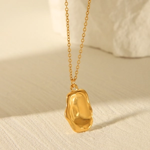 Detailed view of a gold stainless steel necklace with a fan-shaped pendant on textured surface