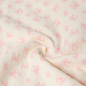 Close-up of soft double-layer cotton gauze fabric with pink bow pattern and tassel detail