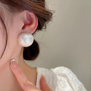 Close-up of elegant textured white pearl stud earrings worn by a model in soft light