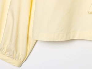 Detail of pale yellow poplin shirt featuring pleated cuffs and neat hem stitching