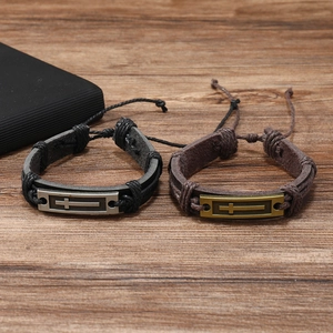 Close-up of black and brown leather braided bracelets with metal cross on wooden surface