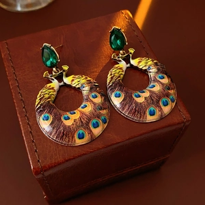 Detail of vintage peacock enamel earrings with green gems on a brown leather case