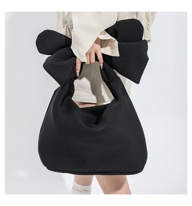 Detail of black puffy nylon handbag featuring a large soft decorative bow on the handle