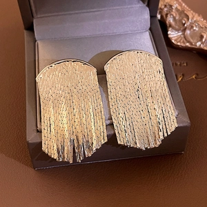 Macro shot of long gold tassel earrings with fan-shaped metal fringe on a jewelry box