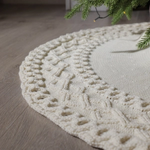 Cream knit Christmas tree skirt with thick cable weave and round design on wooden floor