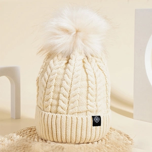 Detail of cable knit pattern and fluffy faux fur pompom on a warm winter beanie