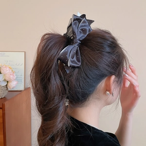 Elegant black satin polka dot bow hair clip shown on a soft ponytail hairstyle