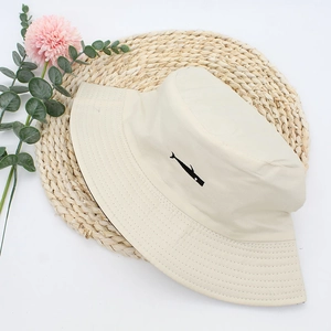 Cream cotton bucket hat with black fish embroidery on woven mat with flowers