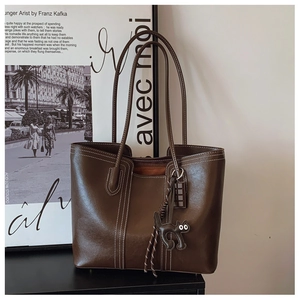 Dark brown leather tote bag with black cat charm placed against artistic poster background