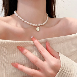Dettaglio collana con perle barocche e ciondolo ovale dorato con incisione di rosa
