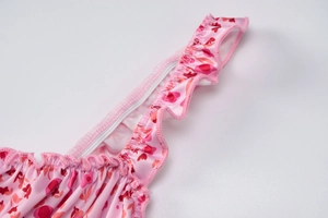 Close-up of pink floral dress strap featuring delicate ruffle details and red flower print