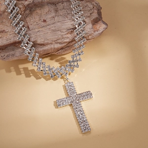 Détail d'un collier croix en argent avec zircons pavés suspendu sur un bloc de bois