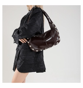 Detail of dark brown glossy leather hobo bag with large silver metal rivets and wide strap