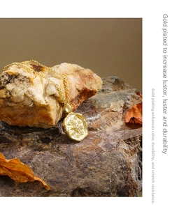 Detailed close-up of golden sunburst coin pendant with zircon stones on stone background