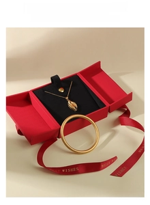 Macro detail of gold leaf necklace and bracelet in a red ribbon gift jewelry box