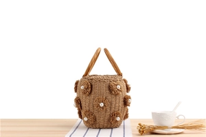 Detail of straw bucket bag with pearl flower accents on a light wooden surface