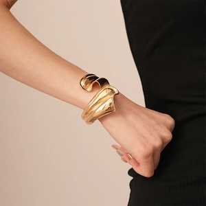 Detail of chunky gold irregular geometric wavy open cuff bracelet on female wrist