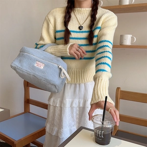 Detailed macro view of a soft light blue plush makeup bag held by a model in a cafe
