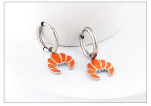 Detail view of silver earrings with orange croissant pendants on white background