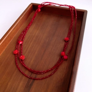 Detail of red beaded multilayer long necklace with rose floral pendant on wooden tray