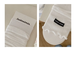 Detail of white ribbed knit leg warmers featuring lettuce trim edges and brand label