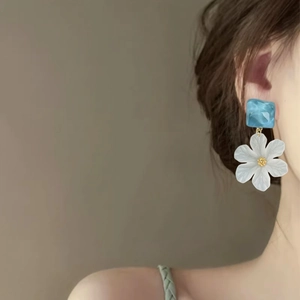 Close-up of elegant acrylic flower earrings with blue square studs on a model's ear