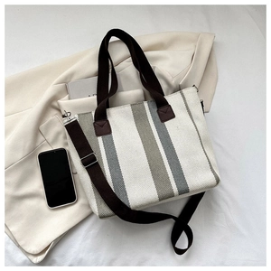 Detail of striped canvas tote bag with brown leather accents on a beige blazer