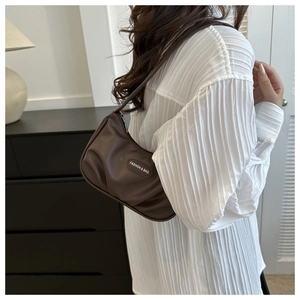 Gros plan du sac baguette en cuir mat marron avec emblème décoratif sur la sangle
