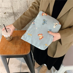 Close-up of light blue corduroy pouch with butterfly embroidery and brand label