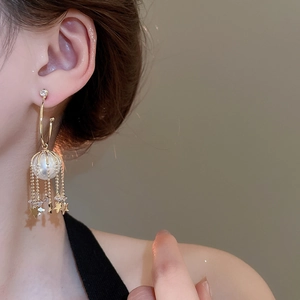 Detail of gold tassel earrings with star charms and pearl in a wire cage frame
