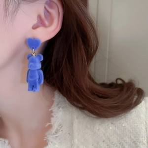 Close-up of blue flocked bear and heart stud earrings worn on a female ear model