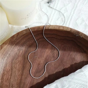 Detailed view of a slender silver snake bone chain necklace on a rustic wooden tray